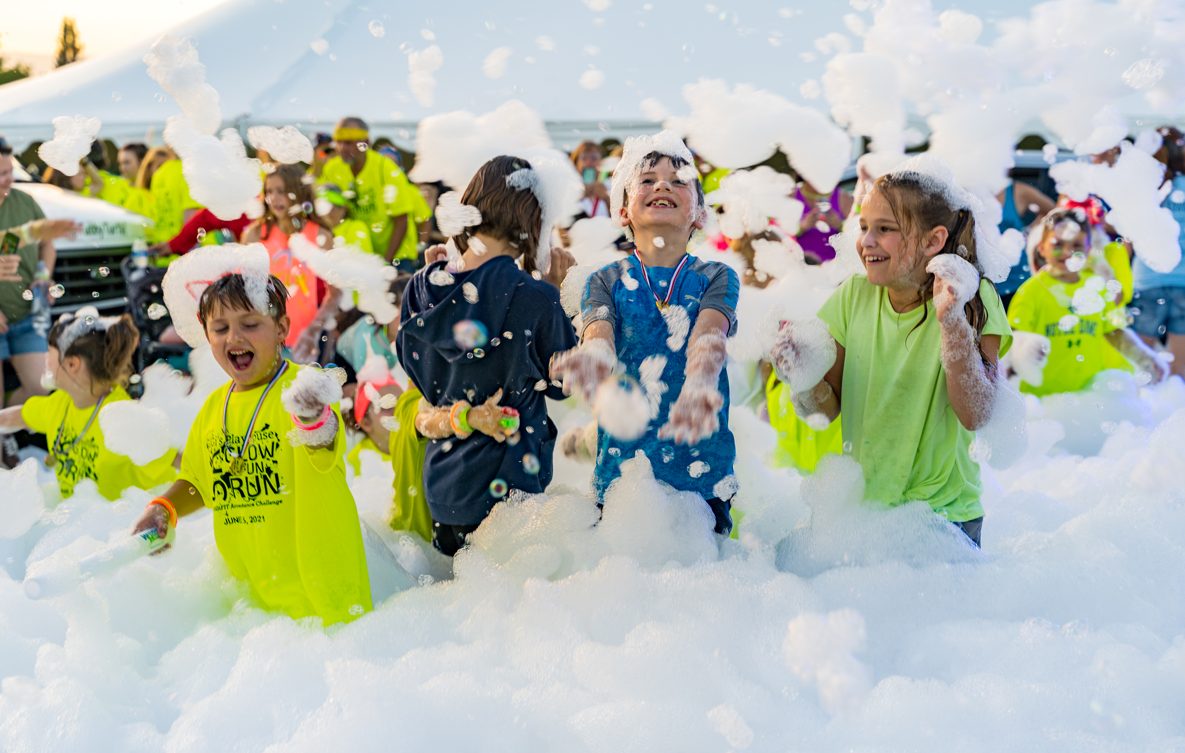 Kids in neon shirts celebrating in deep foam at a fun run
