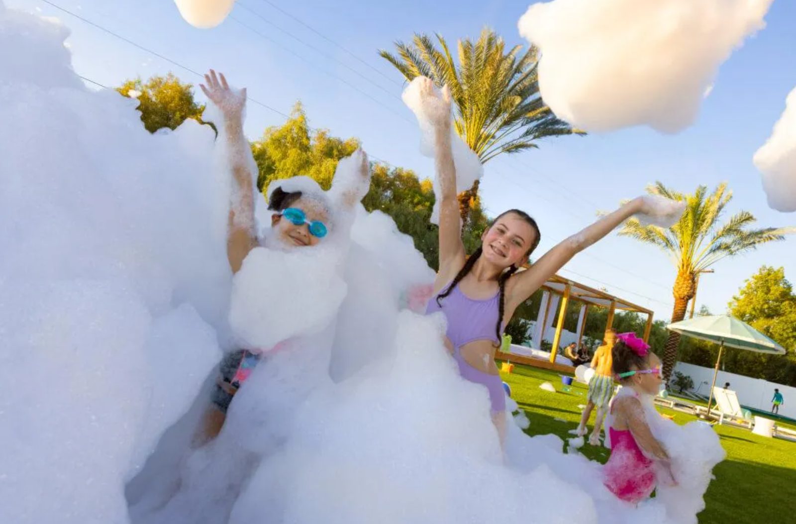 Kids raising their arms in deep foam surrounded by palm trees
